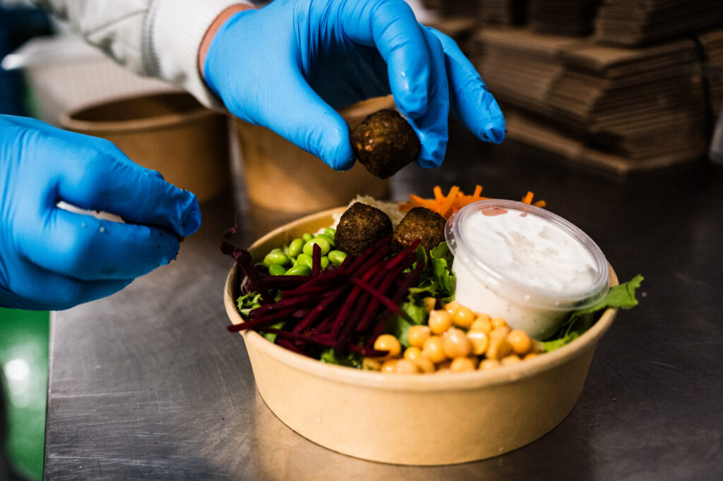 Falafel wird von Hand in eine Salatbowl gelegt